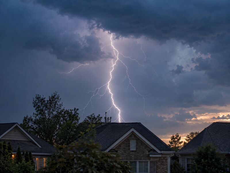 Lightning striking behind suburban rooftops at dusk